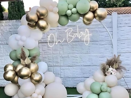 Sage, ivory and gold balloon arch around a backdrop wall with a script neon sign